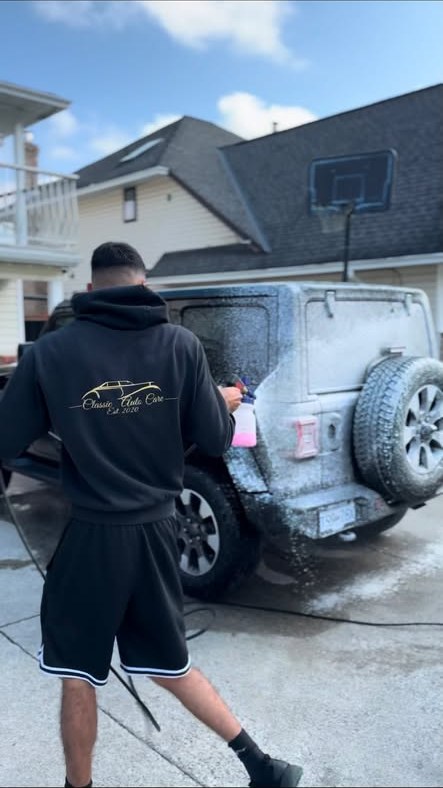 A Classic Auto Care detailer foam-washing a Jeep in a customer's driveway